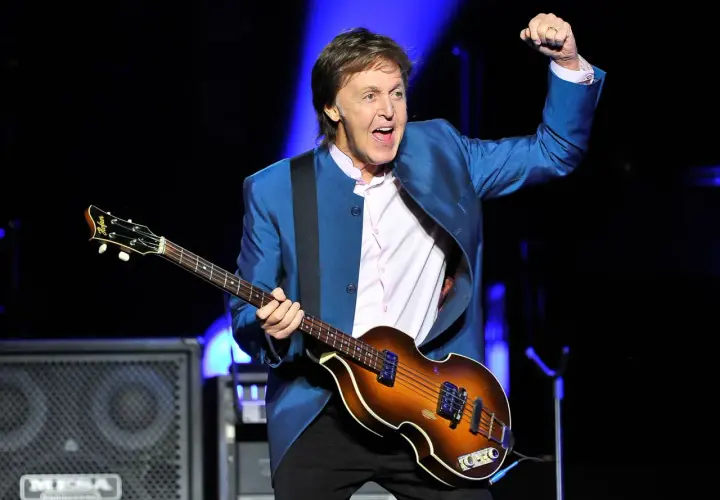 Paul McCartney, icône du rock, joue de sa basse Höfner sur scène, poing levé dans un geste d'enthousiasme.