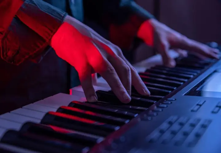 Mains éclairées par la lumière rouge jouant sur les touches d'un piano, créant une ambiance musicale.