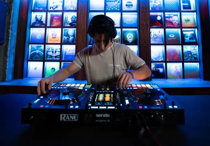 Un DJ mixe sur une console Rane, avec des vinyles rétro éclairés en fond. Fiche technique DJ.