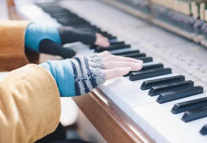 Les doigts de pianiste, vêtus de mitaines colorées, effleurent les touches d'un piano, créant une mélodie douce.