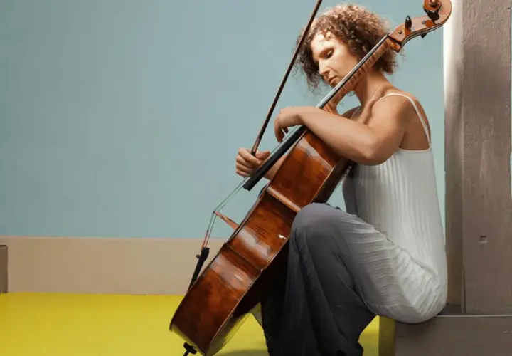 Une jeune femme aux cheveux bouclés s'applique à apprendre le violoncelle, concentrée sur son instrument.