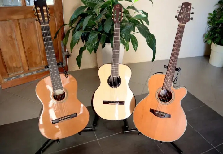 Trois guitares acoustiques sur des pieds, dont une avec une étiquette indiquant une marque de guitare.