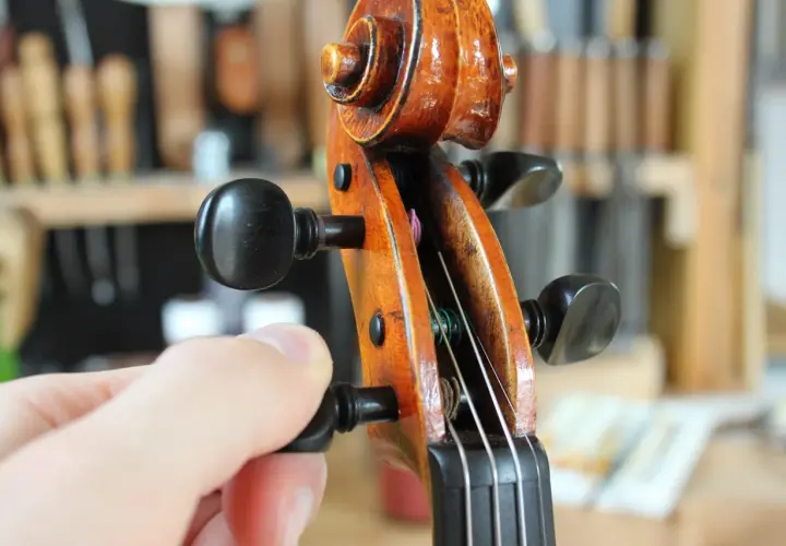 Main d'un musicien ajustant la tension d'une corde pour accorder le violon.