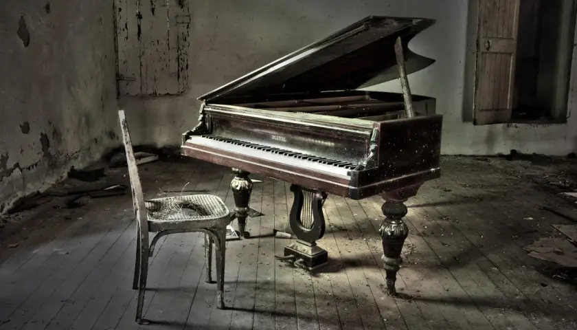Un piano à queue poussiéreux dans une pièce abandonnée, avec une chaise usée. La hauteur du tabouret du piano semble parfaite pour jouer.