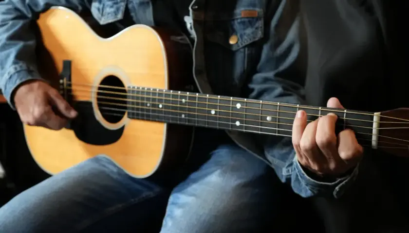 Un guitariste en jean montre comment tenir une guitare, ses doigts formant un accord sur le manche.