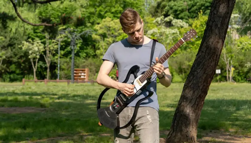 Un homme joue d'une guitare électrique sans ampli dans un parc verdoyant, profitant du beau temps pour faire de la musique en plein air.