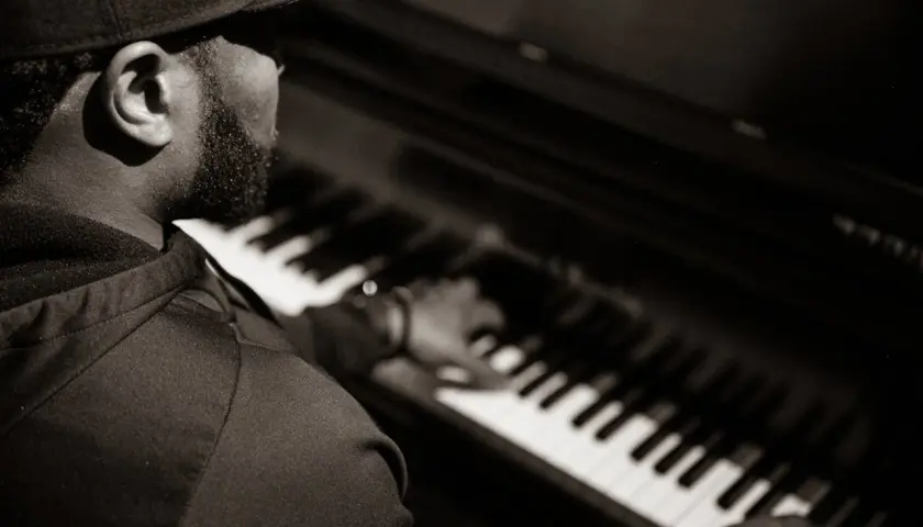 Un pianiste concentré joue un accord au piano, sa main effleurant les touches.