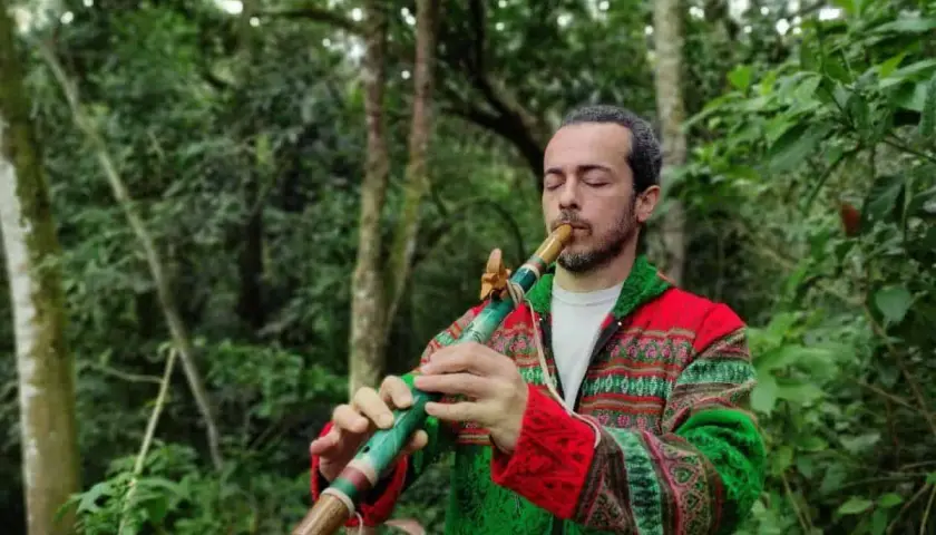 Un homme joue d'un instrument de musique à bec coloré dans une forêt luxuriante.