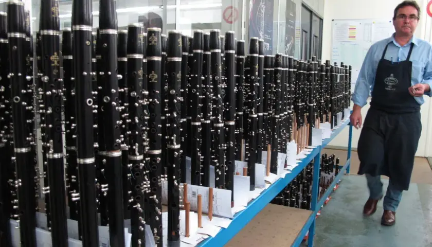 Un homme en tablier inspecte un buffet de clarinettes, prêt à être expédié. Ces instruments de musique, des modèles "crampon mantes", sont alignés sur des étagères.