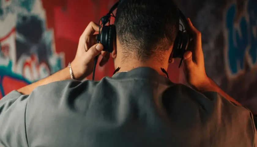 Un homme ajuste un type de casque audio sur ses oreilles, le dos tourné, devant un mur couvert de graffitis colorés.