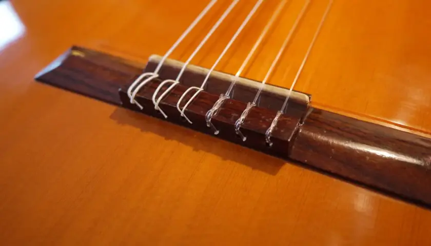 Gros plan sur le chevalet d'une guitare classique, où chaque corde est solidement attachée par un nœud corde guitare classique.