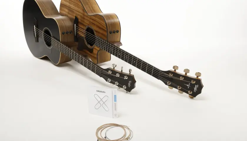 Deux guitares acoustiques, une noire et une en bois naturel, prêtes à produire le son de la guitare. Un jeu de cordes D'Addario est posé devant.