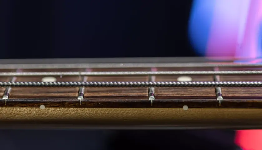 Gros plan sur les cordes et les frettes d'une guitare, révélant le radius subtil du manche.