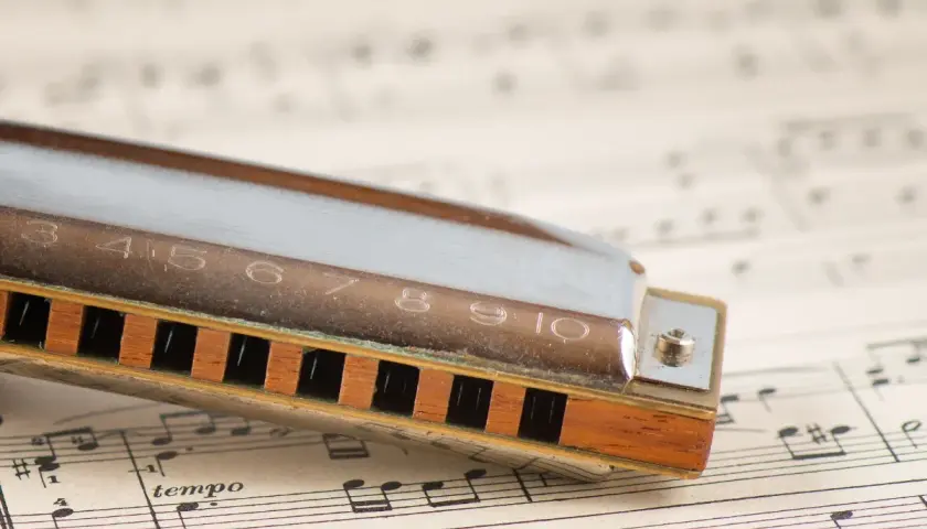Harmonica posée sur une partition de musique. Les notes et le mot "tempo" sont visibles, prêts à accompagner les mélodies de cet instrument.