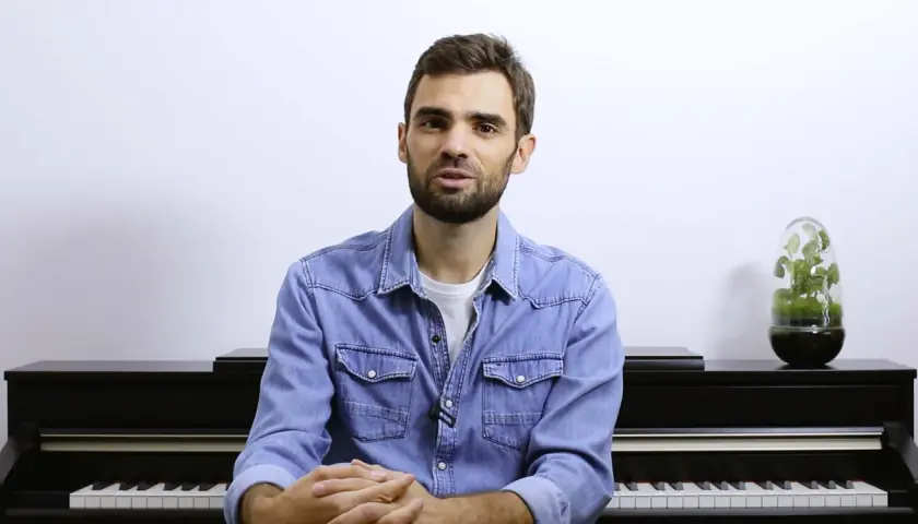 Un homme devant un piano, prêt à jouer. Ses mains sont croisées, attendant le moment de créer de la musique à quatre mains.