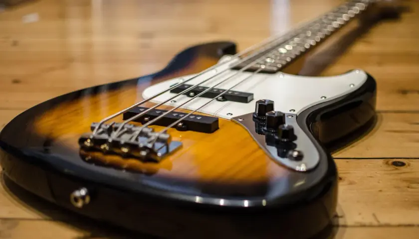 Gros plan sur une basse électrique sunburst posée sur un parquet en bois. Les cordes et les micros sont bien visibles.