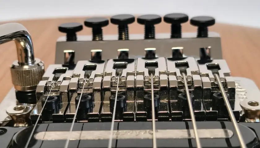 Gros plan sur le chevalet d'une guitare électrique, avec le bras de trémolo visible. Les six pontets chromés sont alignés, prêts à produire des notes vibrantes grâce au système de tremolo.