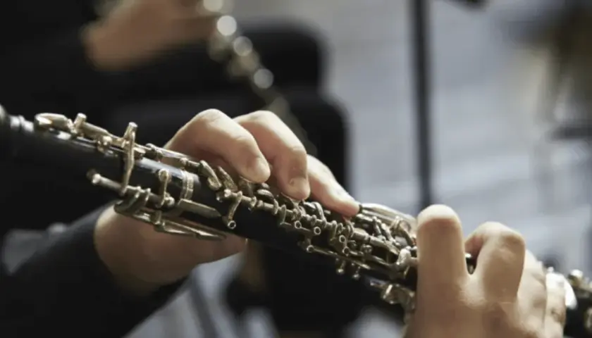Mains jouant d'un hautbois, un instrument à vent aux clés complexes, évoquant la musique classique.