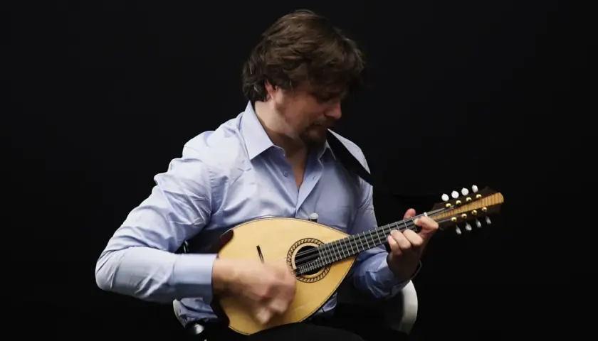 Un homme joue de la mandoline, son visage concentré sur l'instrument. Le son mélodieux de la mandoline emplit la pièce.