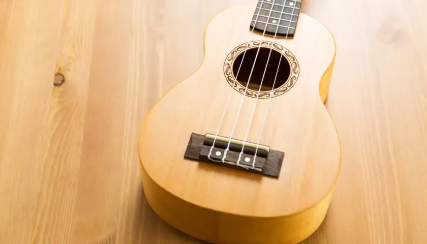 Un joli ukulélé en bois clair, prêt à jouer de la musique sur une table en bois.