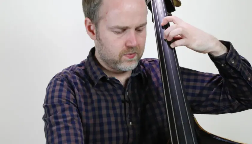 Un musicien joue un arpege basse, ses doigts glissant sur les cordes de la contrebasse.