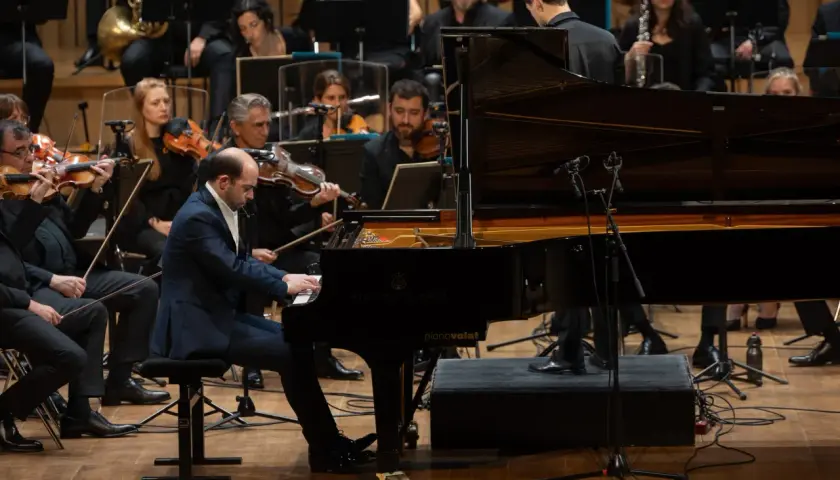 Un pianiste joue un morceau au tempo larghetto, entouré par un orchestre symphonique.