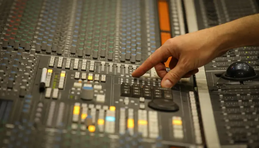 Main d'un ingénieur du son ajustant les faders d'une console de mixage pour un sound check.