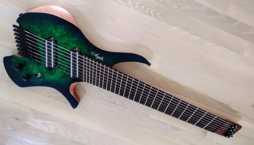 Guitare électrique Agile multiscale vert émeraude, avec 9 cordes et un manche fin, posée sur un parquet clair.
