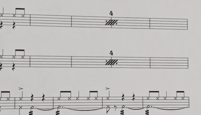 Partitions musicales avec des notes de batterie et des indications de tempo. Le symbole de répétition musique est présent, suggérant une section à rejouer.