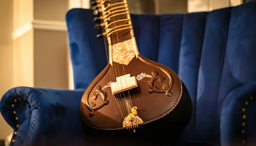 Un magnifique sitar indien repose sur un fauteuil bleu profond, prêt à faire vibrer ses cordes.