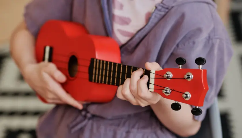 Enfant jouant d'un petit instrument de musique rouge vif, un ukulélé, avec concentration.
