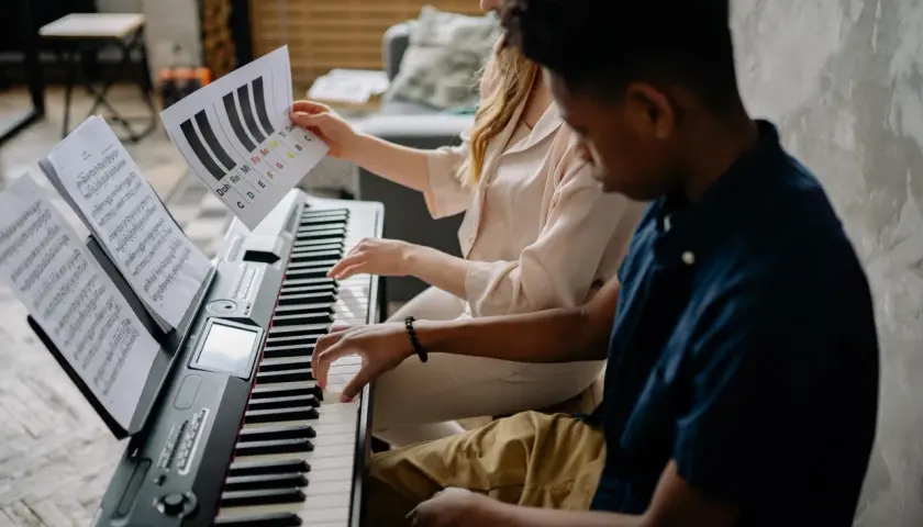 Deux mains jouent sur un piano, l'une suit une partition, l'autre une feuille avec des notes comme sol#m.