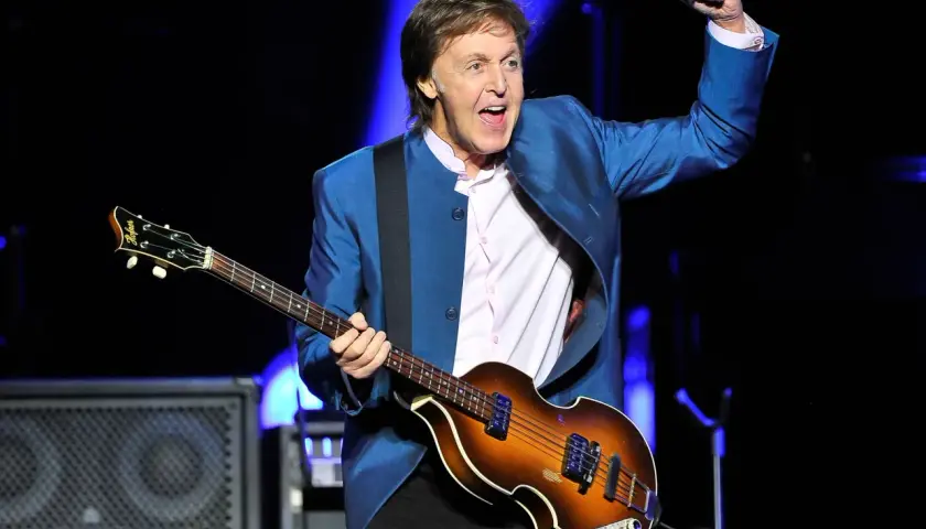 Paul McCartney, icône du rock, joue de sa basse Höfner sur scène, poing levé dans un geste d'enthousiasme.