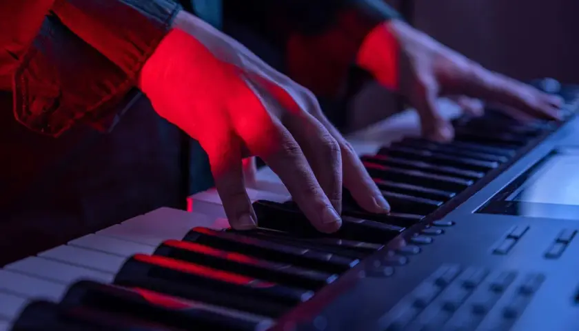 Mains éclairées par la lumière rouge jouant sur les touches d'un piano, créant une ambiance musicale.