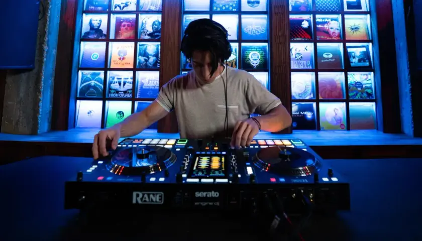 Un DJ mixe sur une console Rane, avec des vinyles rétro éclairés en fond. Fiche technique DJ.