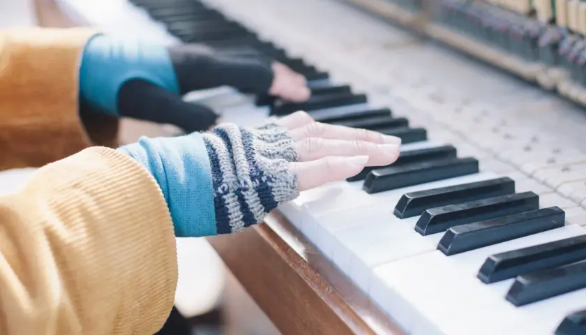 Les doigts de pianiste, vêtus de mitaines colorées, effleurent les touches d'un piano, créant une mélodie douce.