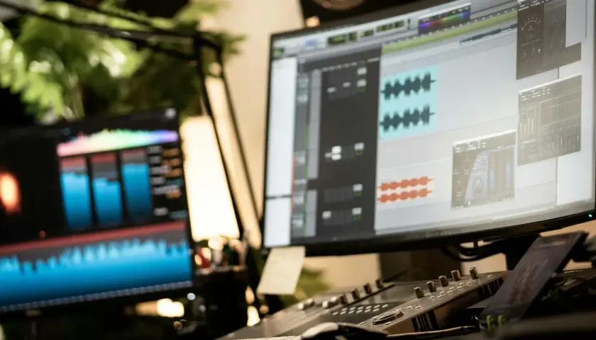 Post-production audio, avec des formes d'onde et des pistes sur écran. Un léger micro-bleed de lumière sur le côté gauche.