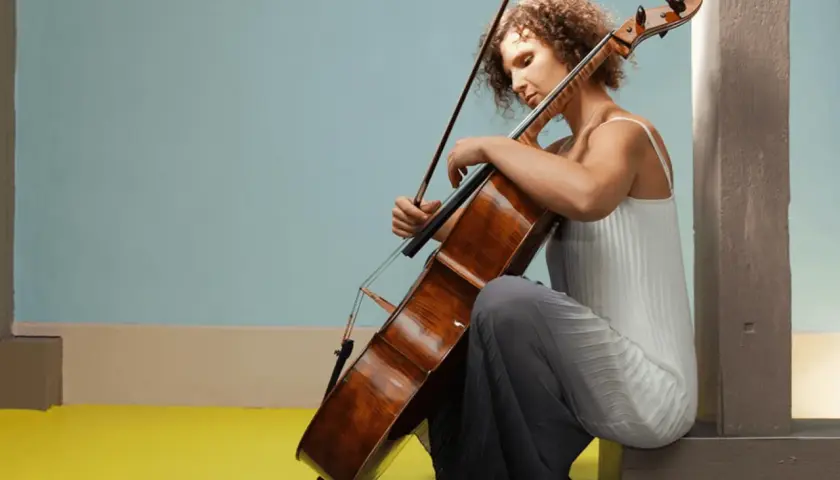 Une jeune femme aux cheveux bouclés s'applique à apprendre le violoncelle, concentrée sur son instrument.