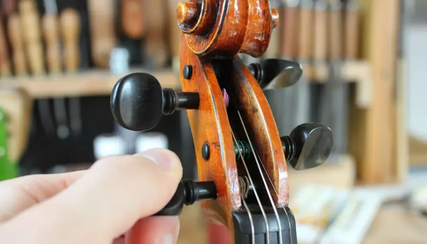 Main d'un musicien ajustant la tension d'une corde pour accorder le violon.