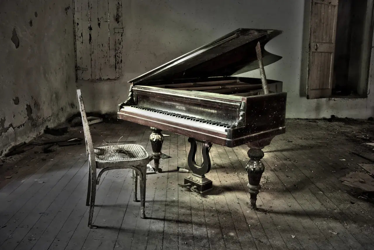 Un piano à queue poussiéreux dans une pièce abandonnée, avec une chaise usée. La hauteur du tabouret du piano semble parfaite pour jouer.