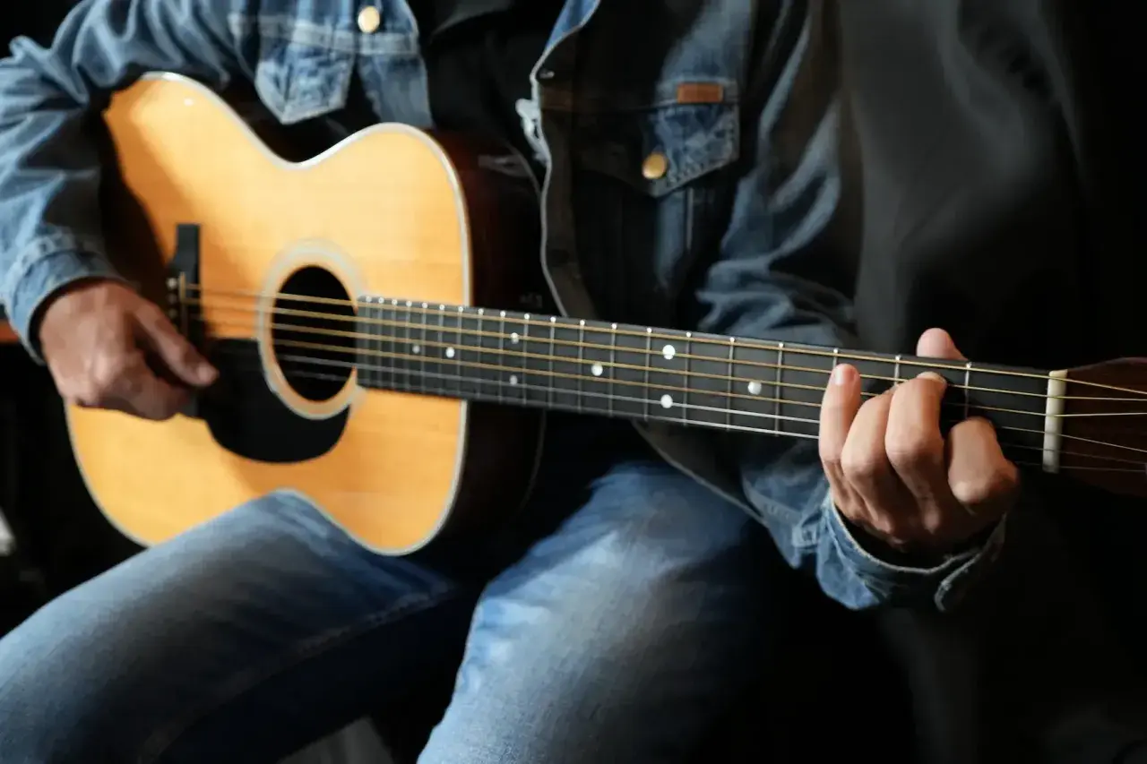 Un guitariste en jean montre comment tenir une guitare, ses doigts formant un accord sur le manche.