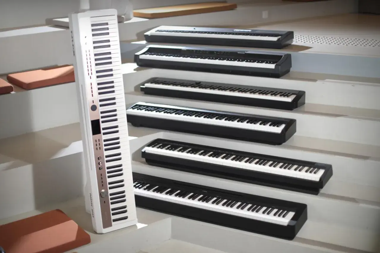 Une rangée de claviers de piano numérique ou acoustique, certains blancs, d'autres noirs, disposés en escalier.
