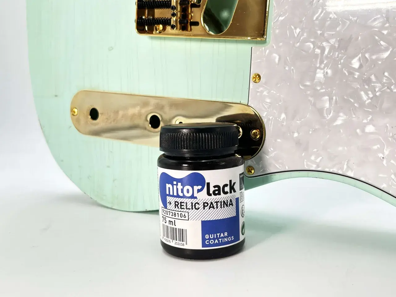 Flacon de "nitorlack relic patina" à côté d'une guitare électrique couleur menthe, prête pour un relicage guitare.