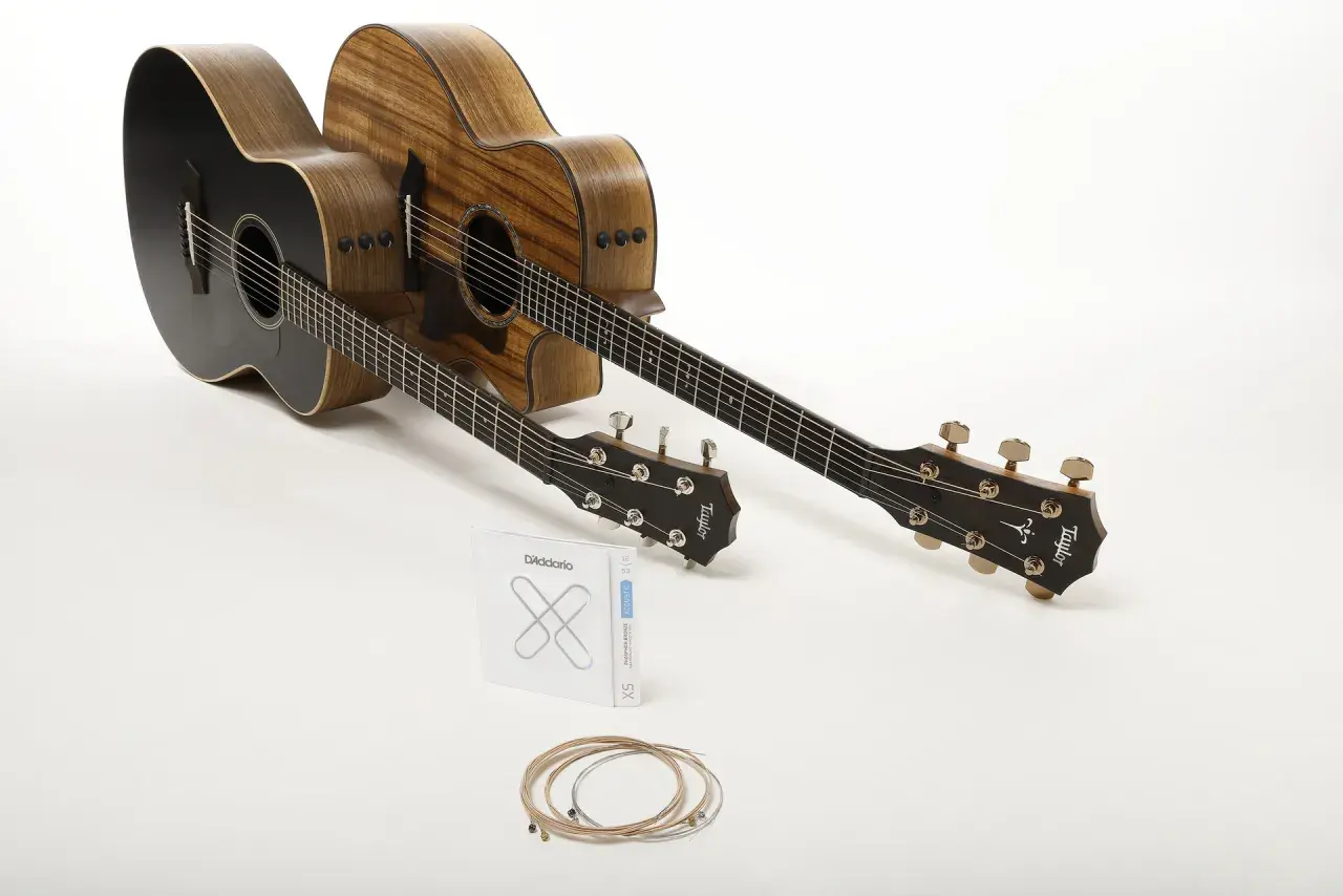 Deux guitares acoustiques, une noire et une en bois naturel, prêtes à produire le son de la guitare. Un jeu de cordes D'Addario est posé devant.