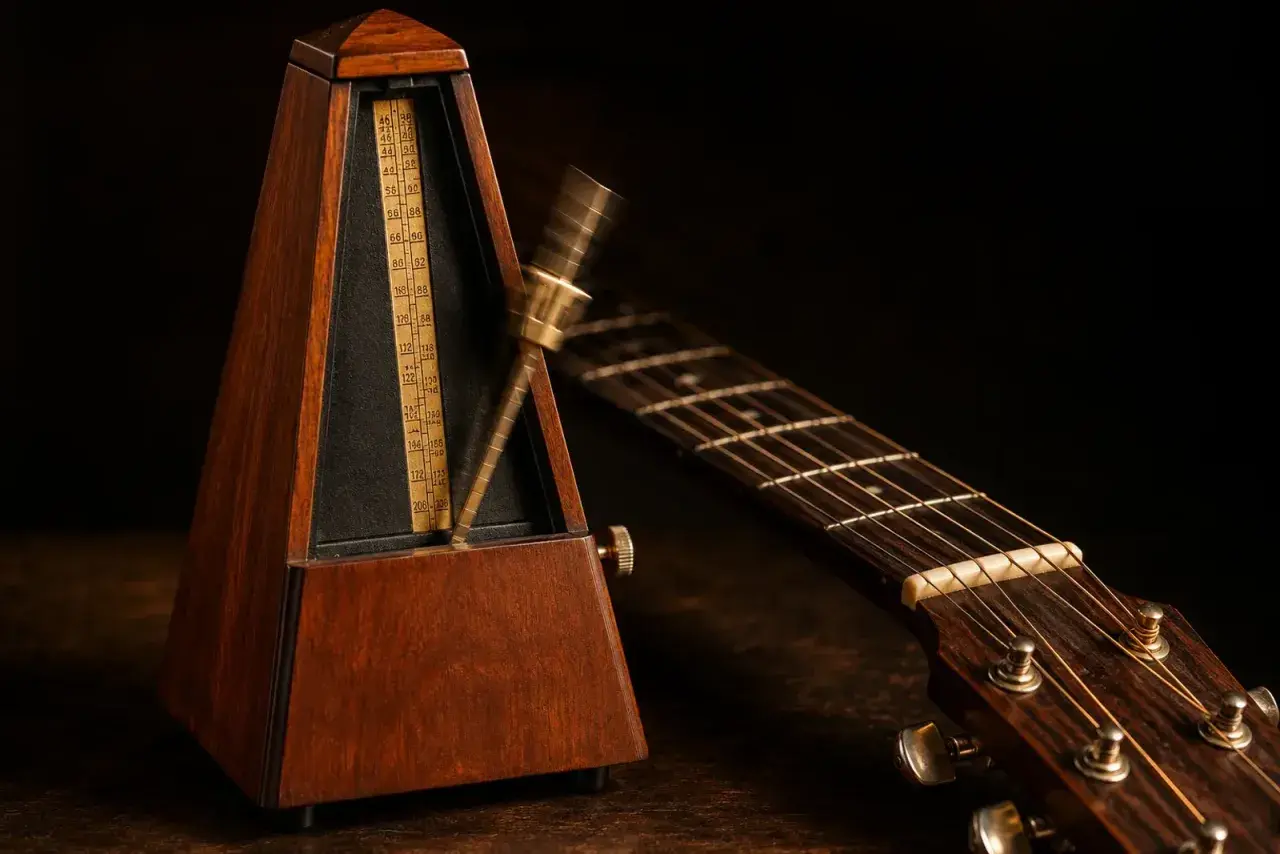 Un métronome en bois, outil essentiel pour la définition du tempo musical, oscille près d'une guitare acoustique.