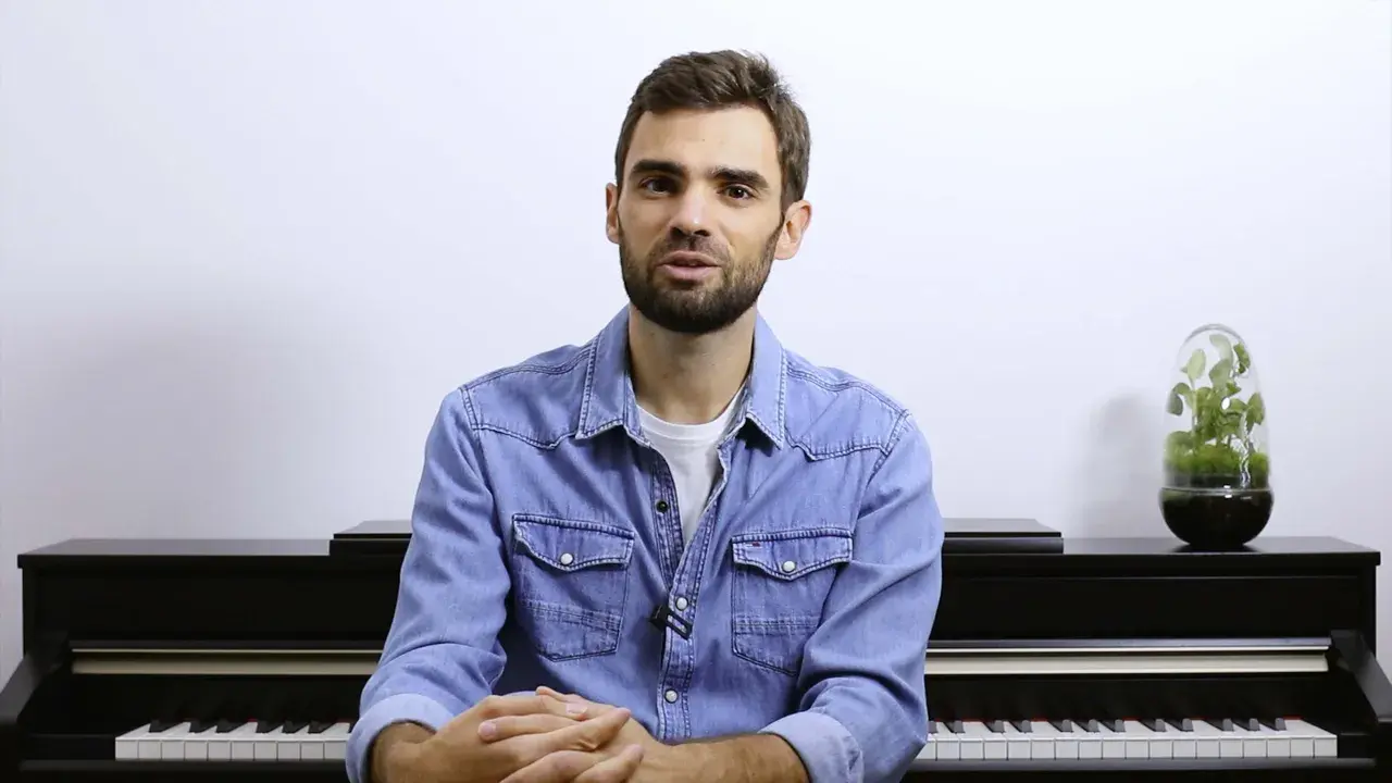 Un homme devant un piano, prêt à jouer. Ses mains sont croisées, attendant le moment de créer de la musique à quatre mains.
