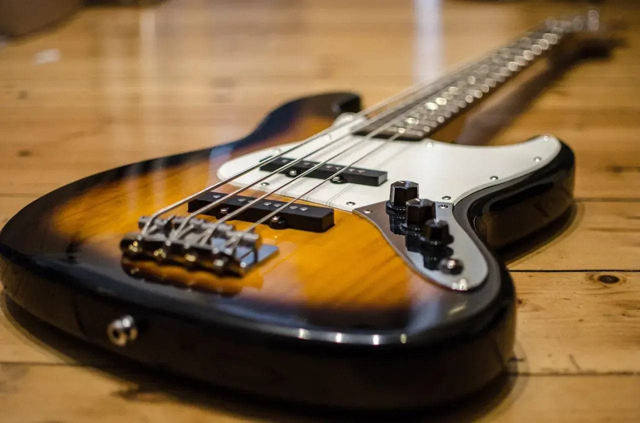 Gros plan sur une basse électrique sunburst posée sur un parquet en bois. Les cordes et les micros sont bien visibles.