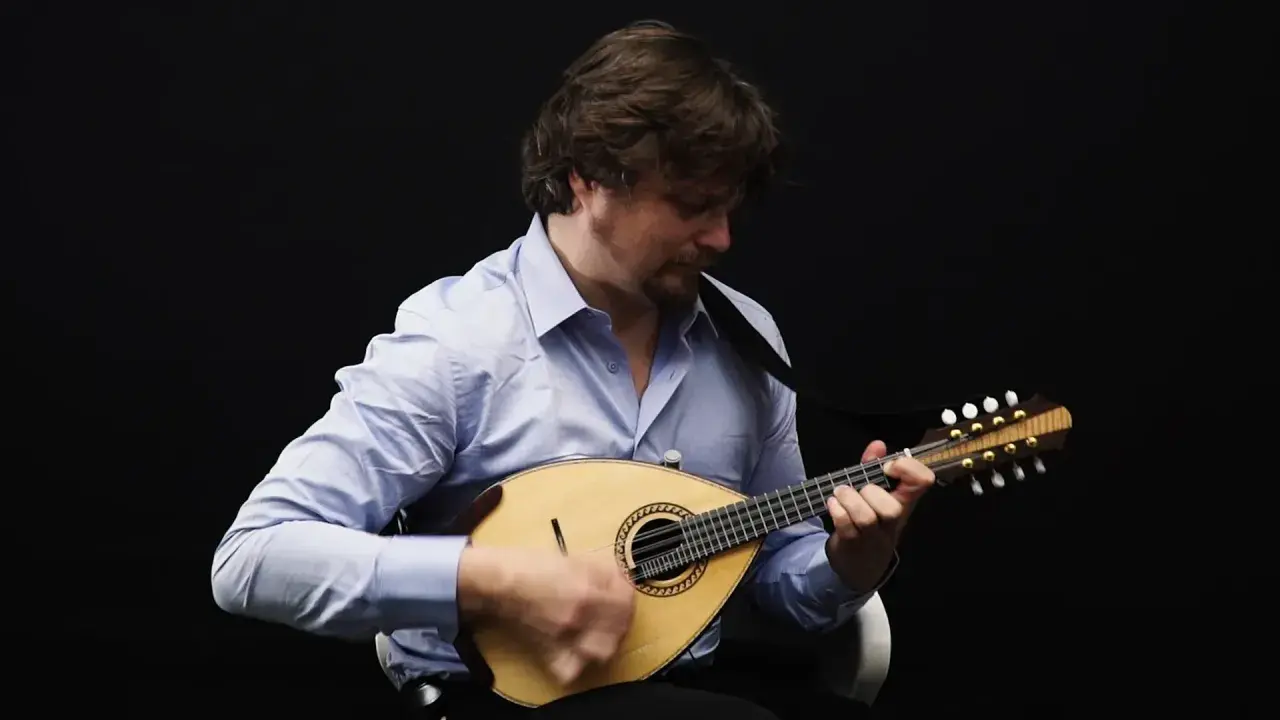 Un homme joue de la mandoline, son visage concentré sur l'instrument. Le son mélodieux de la mandoline emplit la pièce.