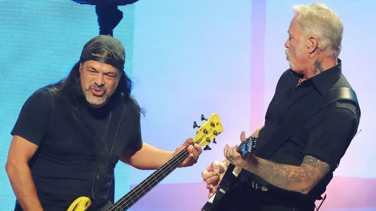 Robert Trujillo, bassiste de Metallica, joue avec passion sur scène, son instrument jaune vif contrastant avec le fond bleu.