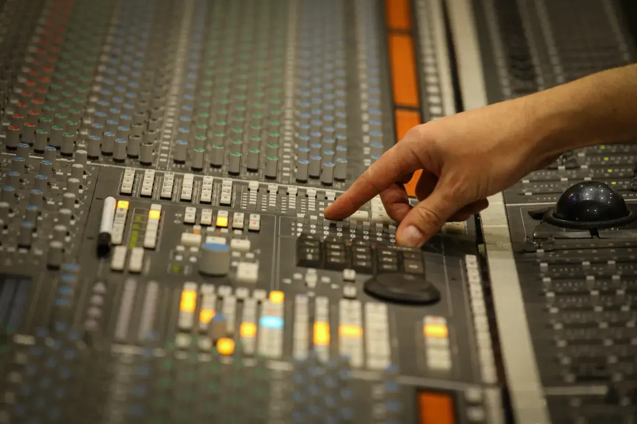 Main d'un ingénieur du son ajustant les faders d'une console de mixage pour un sound check.